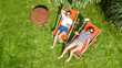 © Iuliia Sokolovska - Young girls relax in summer garden in sunbed deckchairs on grass, women friends have fun outdoors in green park on weekend, aerial drone view from above