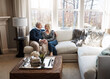 © BuyoutReese09/peopleimages.com - Smile, holding hands and senior couple at house with love, partner affection and bonding together. Happy, elderly people and embrace with admiration, retirement and relationship commitment in lounge
