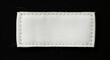 © sahenur89 - Blank white rectangular fabric clothing label sewn on black textile background, close-up