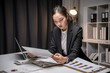 © Apichat - Asian businesswoman analyzing business data reports late at night