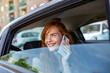 © Graphicroyalty - Redhead woman talking on phone in car. Happy female passenger with freckles using smartphone. Communication and transportation concept. Beautiful ginger girl smiling on a call in taxi back seat.