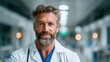 © Dulemegapixel - A confident, bearded male doctor dressed in a white coat poses with a gentle smile in a hospital environment, embodying professionalism, trust, and care for patients.