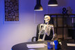 © Pixel-Shot - Human skeleton model sitting in office at night