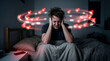 © ZaStock - Man sits in bed with hands on head while looking stressed by notifications around him. Dark room with minimal light creates an atmosphere of anxiety