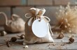 © Vadym - Natural linen pouch with blank round tag on rustic wood table. Boho decor, dry plants, pinecones. Ready for gift personalization or product branding.