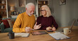 © Stockphotodirectors - A couple engages in a discussion about life insurance plans while sitting at a table. They use a tablet, calculator, and papers to organize their financial decisions in a cozy living room.