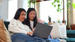 © luisrojasstock - Asian female friends using laptop together on sofa