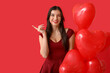 © Pixel-Shot - Beautiful young woman with kiss marks on her face and heart shaped air balloons pointing at something on red background