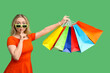 © Pixel-Shot - Young woman in sunglasses holding shopping bags and showing silence gesture on green background