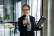 © standret - Businesswoman with short hair in a black suit holds a microphone and tablet while speaking in a modern office with large windows and a conference table