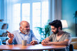 © StockImageFactory - Indian Elderly dad guiding his grown son in a thoughtful family moment indoors.