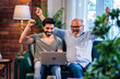 © StockImageFactory - Indian retired dad and grown son celebrating profit using laptop indoors