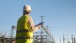 © DawDunia - Engineer wearing safety vest and hard hat, working at a power station, using a digital tablet for inspection and monitoring electricity grid infrastructure and energy distribution