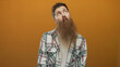 © Krakenimages.com - Man with long beard wearing checkered shirt making a pursed lip gesture in an orange studio; curiosity.