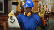 © Krakenimages.com - Man construction worker holding moneybag in church, wearing blue hardhat and gloves, smiling and making ok gesture; confidence prosperity success.