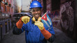 © Krakenimages.com - Man construction worker in blue hardhat holding cuban flag points finger to flag on street amid graffiti lined alley and parked car; pride resilience solidarity.