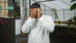© Krakenimages.com - Hispanic man covers face with hands and ring visible inside greenhouse building; introspection solitude.