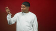 © Krakenimages.com - Man with beard wearing white long sleeve shirt points finger and snaps hand in photo studio against red seamless backdrop, slight smile; playful energy.