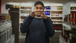 © Krakenimages.com - Man with beard points both fingers at camera in a liquor store aisle inside a building, smiling and engaging shoppers; friendly invitation.