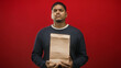 © Krakenimages.com - Man holds brown paper bag with both hands in studio, standing centered against red backdrop with neutral pose and direct gaze; uncertainty duty.