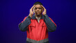 © Krakenimages.com - Hispanic man worker in red safety uniform covers face with hands and palms visible, standing center frame with reflective stripe in a studio; frustration introspection.