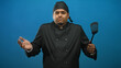 © Krakenimages.com - Man chef in black uniform and skullcap holding a spatula, shrugging shoulders and smiling in studio midshot; cheerful hospitality.
