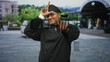 © Krakenimages.com - Hispanic man chef in black uniform holds spatula and forms l with hand on forehead in front of station building; playful confidence.