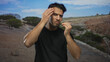 © Krakenimages.com - Young hispanic man outdoors in arid landscape touching his face with mountains and clear blue sky in the background showing contemplation and focus