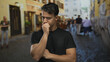© Krakenimages.com - Young hispanic man appearing thoughtful on a busy city street in an outdoor urban setting, surrounded by blurred pedestrians and rustic buildings.