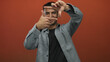 © Krakenimages.com - Young hispanic man making frame gestures with hands on an isolated red background, expressing creativity and focus in a filmmaking or photography context.