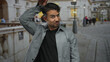 © Krakenimages.com - Young man outdoors performing playful rabbit ear gesture on a bustling city street with blurred buildings and people in the background, highlighting his joyful expression and urban environment.