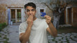 © Krakenimages.com - Hispanic man outdoors examining credit card with surprised expression against rustic building background, suggesting unexpected financial situation or card discovery.