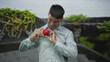 © Krakenimages.com - Smiling young hispanic man in light blue shirt holds bright red heart with hands in green park; affection.