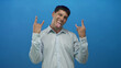 © Krakenimages.com - Young hispanic man sticks out tongue and shows rock horns with both hands in a studio against a blue backdrop; excitement.