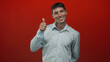 © Krakenimages.com - Young hispanic man gives thumbs up gesture in red studio wearing light blue shirt and smiling broadly; confidence.