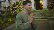 © Krakenimages.com - Young hispanic man wearing sweater with hands pressed together on stone street stairs under festive lights; calm reflection gratitude.