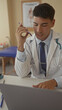 © Krakenimages.com - Man doctor in white coat with stethoscope holds purple smartphone to mouth at desk beside laptop in building; duty.