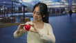 © Krakenimages.com - Woman smiling outdoors holding red heart shape on urban street reflecting happiness and health emphasizing love with a blurred city background creating a lively scene.