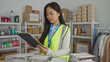 © Krakenimages.com - Woman in reflective vest at charity center inspects donations using tablet surrounded by supplies emphasizing volunteer spirit indoors.