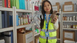 © Krakenimages.com - Woman in reflective vest holding stuffed animal in charity donation center filled with boxes and hygiene products, showcasing volunteer work in indoor setting.