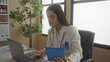 © Krakenimages.com - Hispanic woman doctor in uniform with stethoscope using tablet and laptop in a clinic room displaying a professional healthcare environment indoors.