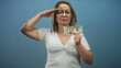 © Krakenimages.com - Hispanic senior woman with grey hair and glasses holds a twenty banknote with hand at chest and salutes in studio; determination.