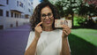 © Krakenimages.com - Woman smiling while holding mexican pesos in an urban outdoor setting, showcasing a middle-aged hispanic female enjoying financial success on the street.