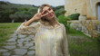 © Krakenimages.com - Young woman flashing a peace sign with her hand by her face in front of a stone building and a paved path; playful joy.