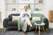 © New Africa - Senior woman knitting with needles on sofa at home