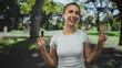 © Krakenimages.com - Woman holding makeup brush, fingers forming a peace sign with hand near face in a park forest with trees and blurred walkers; playful self care.