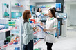 © DC Studio - Pharmacist with clipboard advises female client on suitable supplements during prescription consultation in local drugstore. Medical expert discussing health wellness products with woman in pharmacy.