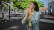 © Krakenimages.com - Young hispanic woman clapping hands in a denim jacket on a sunny city street near a building with trees and sidewalk shadows; happiness gratitude celebration.