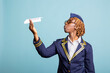 © DC Studio - Black airline stewardess with glasses blows air at diy aircraft, enjoying fun and lighthearted moment against isolated background. Playful air hostess in uniform playing with paper airplane in studio.