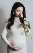 © Nataliya - Portrait of a beautiful pregnant Caucasian girl in a knitted dress inhaling the scent of a rose.